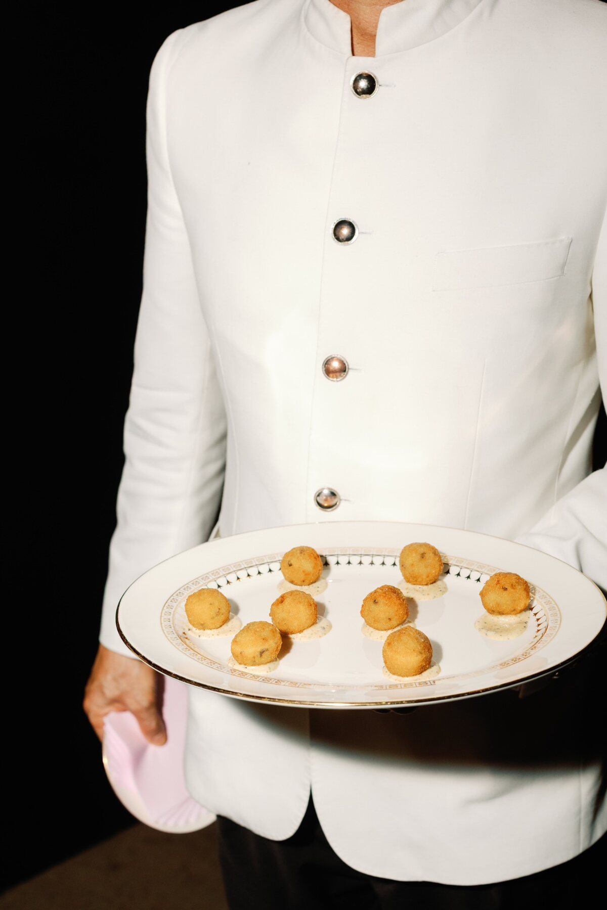 Server in a white jacket presenting plated bites at a Headliner gathering
